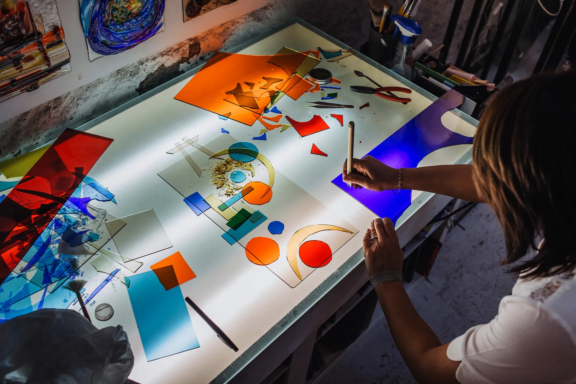 travail en cours, du verre de couleur découpé en formes géométriques est disposé sur une table lumineuse
