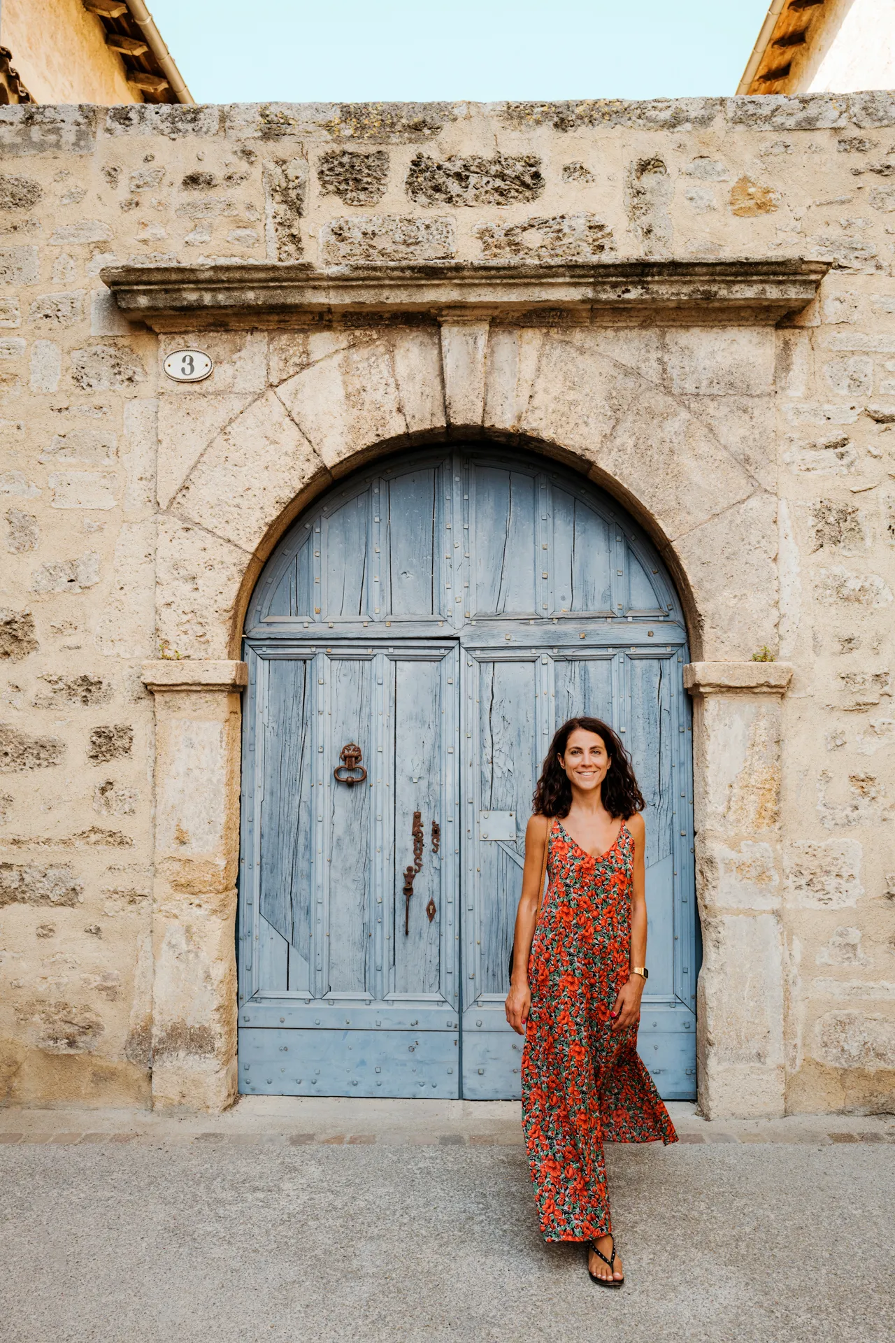 femme en robe rouge devant porte bleue de Pézenas