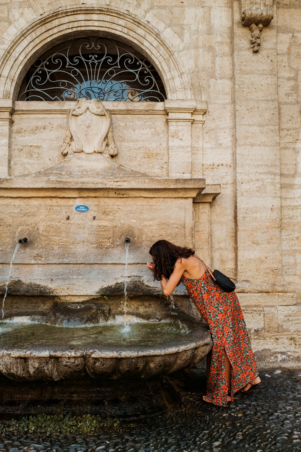 une femme se rafraîchit à une fontaine ancienne de Pézenas